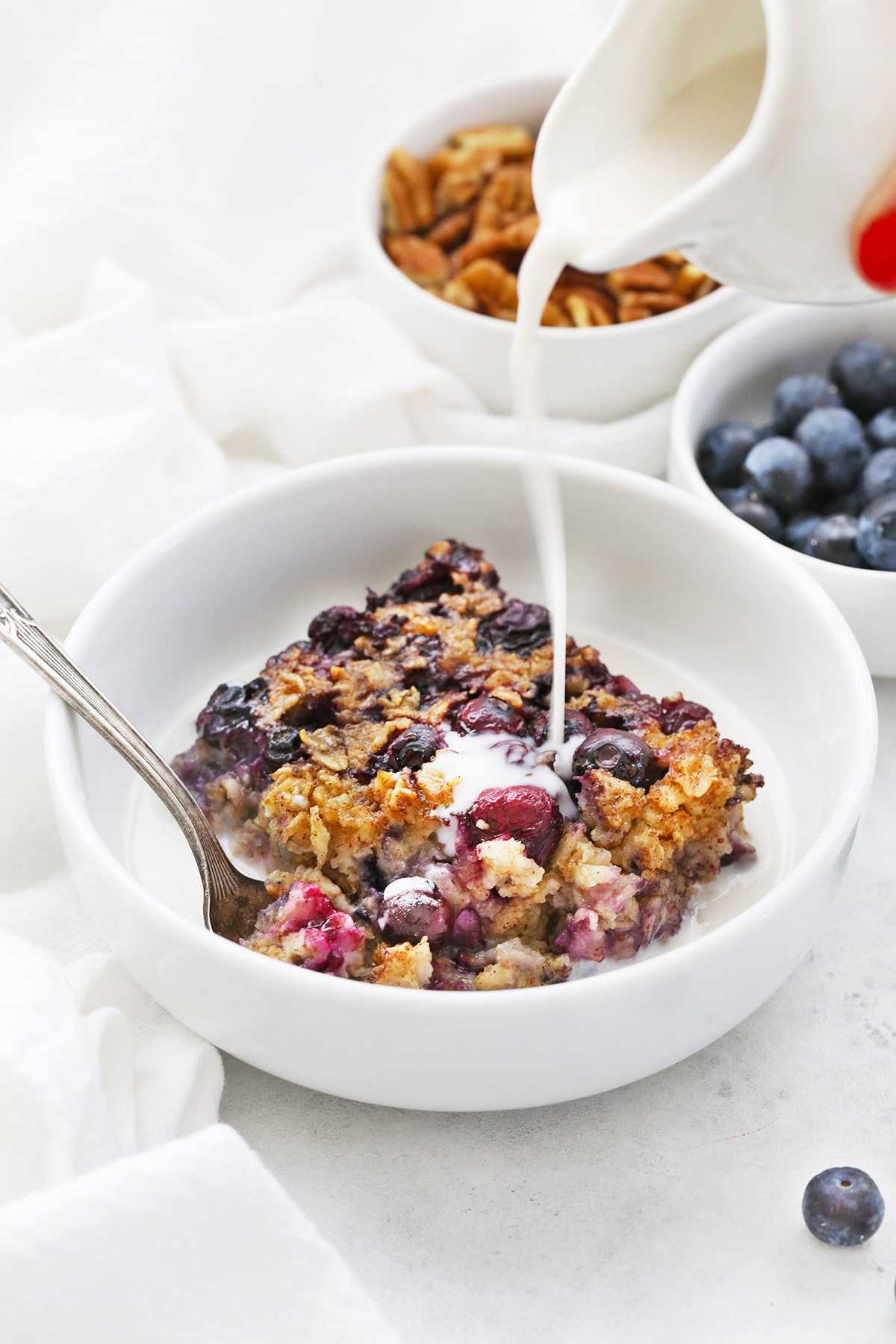 Pouring almond milk over a bowl of blueberry baked oatmeal. 