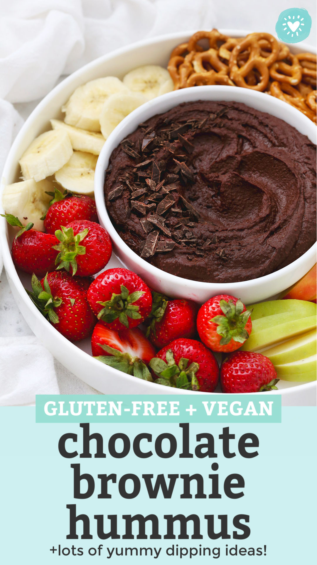 Front view of a bowl of chocolate brownie hummus on a fruit plate with text overlay that reads "Gluten-Free + Vegan Chocolate Brownie Hummus +lots of yummy dipping ideas"