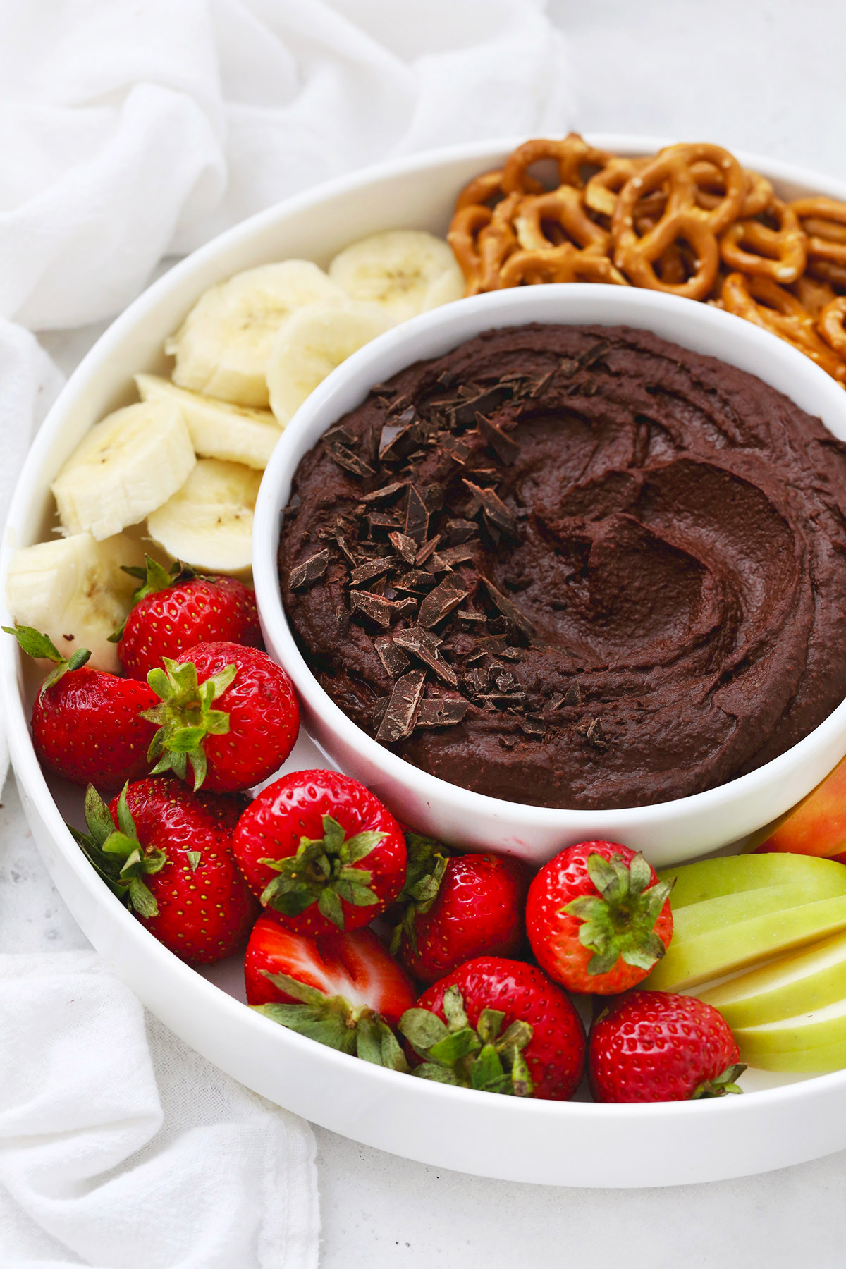 Front view of a bowl of chocolate brownie hummus on a fruit plate