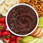 Overhead view of a bowl of chocolate brownie hummus on a fruit plate