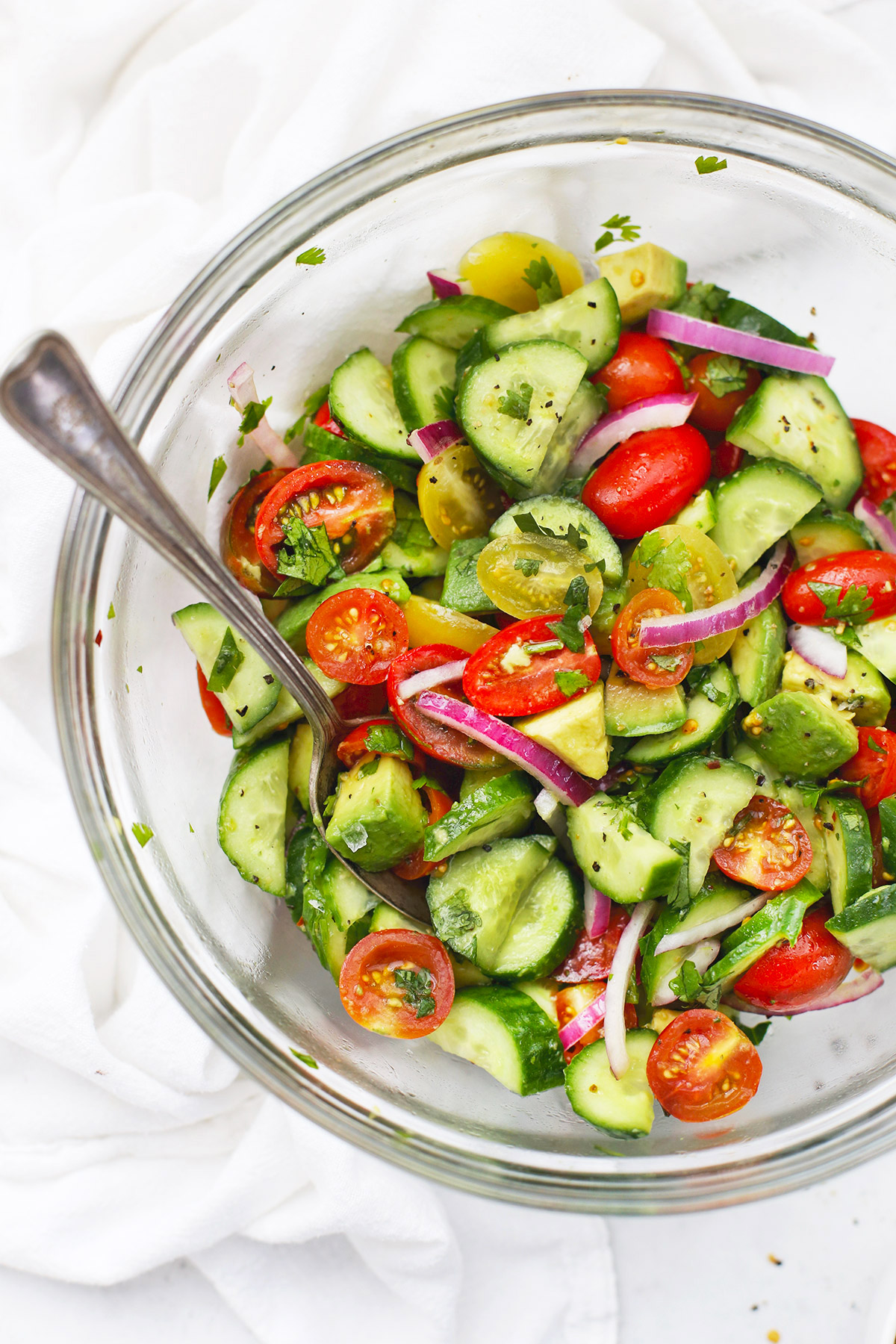 Close up overhead view of a glass bowl of avocado cucumber tomato salad
