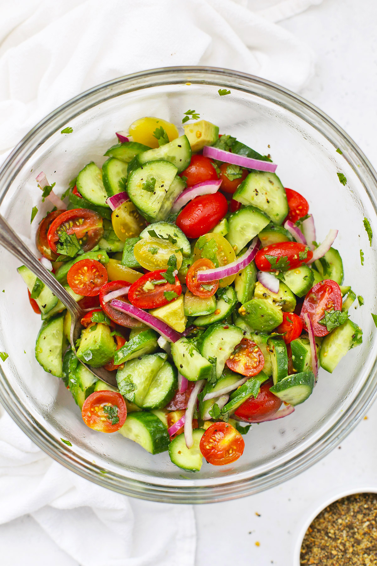 Close up overhead view of a glass bowl of avocado cucumber tomato salad