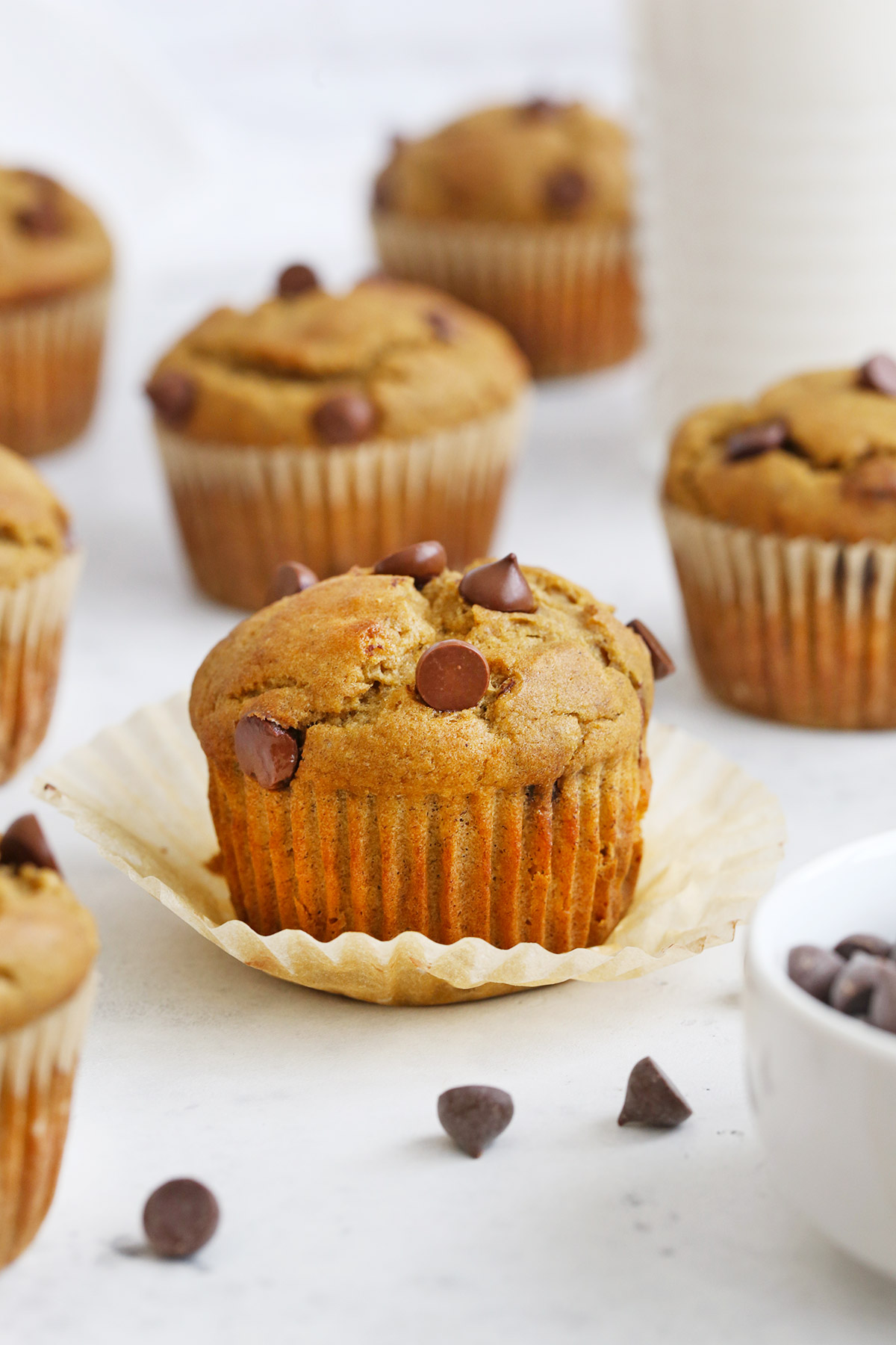 Gluten-Free Chocolate Chip Banana Muffins on a white background with chocolate chips scattered around them. 