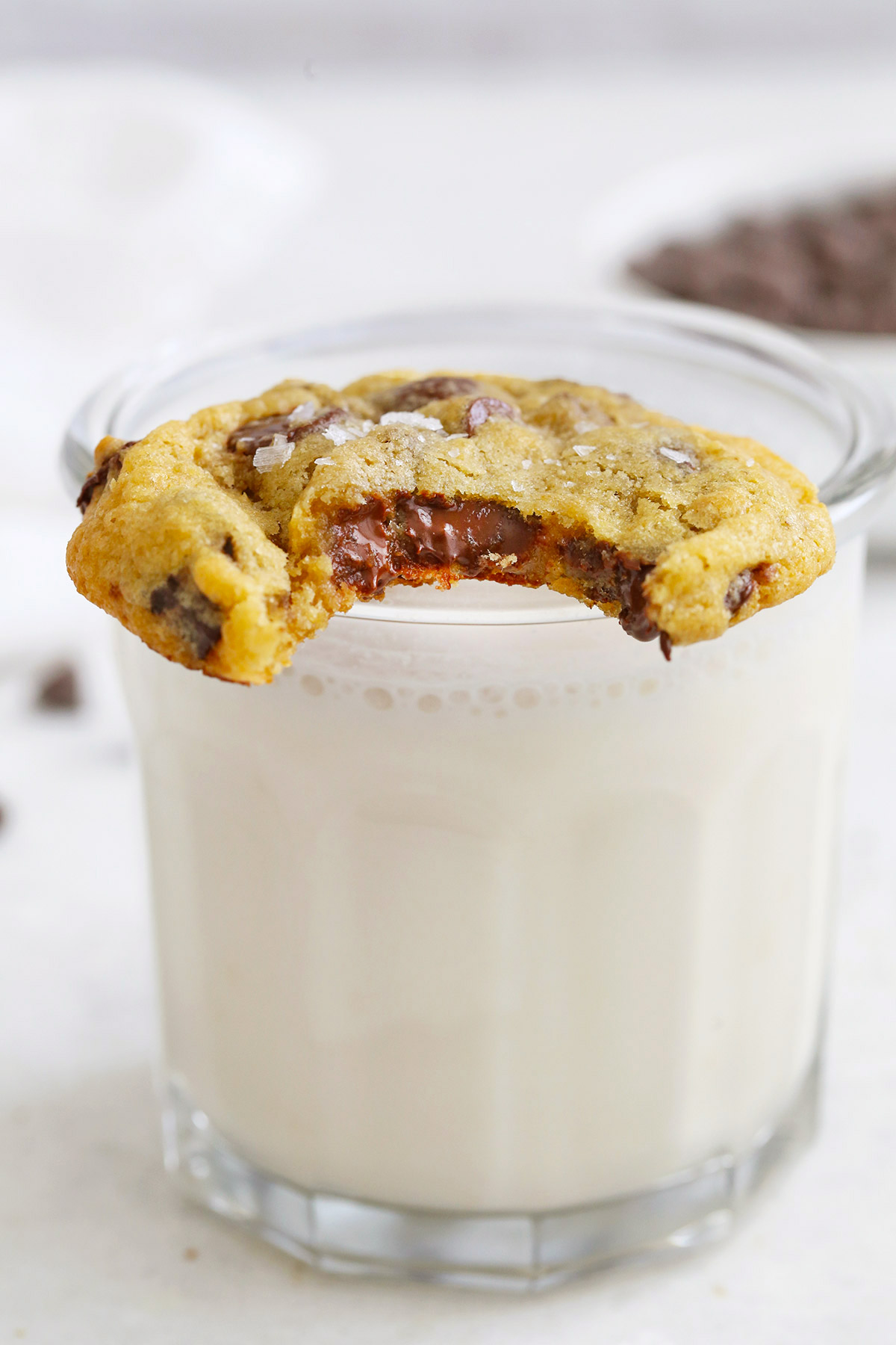 Front view of gluten-free chocolate chip cookie with a bite out of it resting on a glass of almond milk