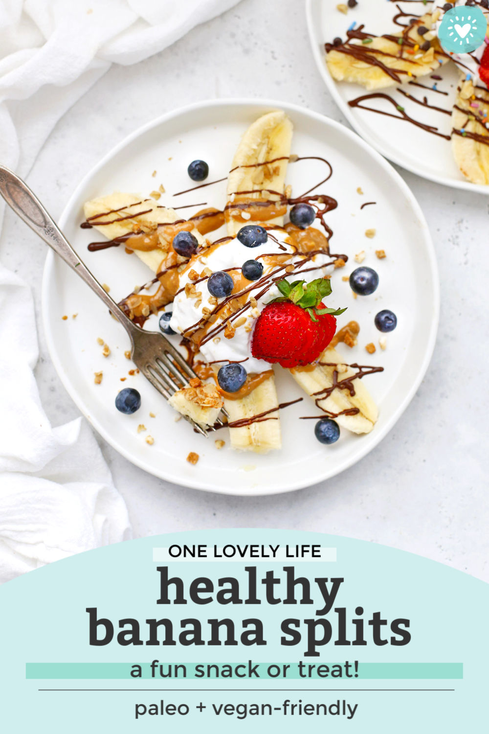 Healthy Banana Split with Yogurt, Peanut Butter, Chocolate, and berries on a white plate with text that reads "One Lovely Life. Healthy Banana Splits--a fun snack or treat! Paleo + vegan-friendly"