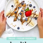 Healthy Banana Split with Yogurt, Peanut Butter, Chocolate, and berries on a white plate with text overlay that reads "Paleo + Vegan-Friendly Healthy Banana Splits. Such a fun snack or treat!"
