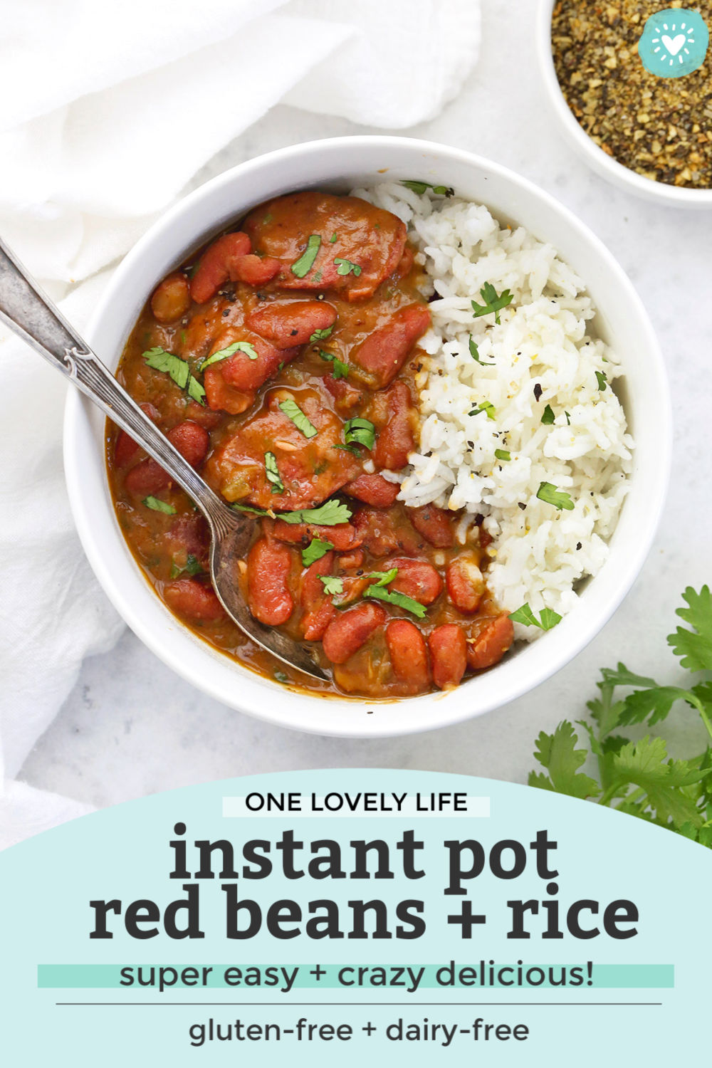 Overhead view of Instant Pot Red Beans and Rice in a bowl garnished with fresh herbs with text overlay that reads "One Lovely Life Instant Pot Red Beans + Rice. Super Easy + Crazy Delicious! Gluten-free + dairy-free"
