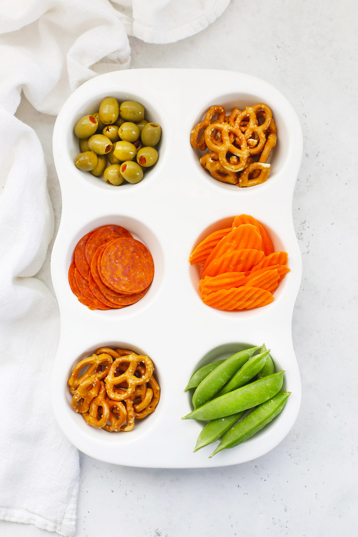 Muffin Tin Snack Tray For Kids with Green Olives, Gluten-Free Pretzels, Pepperoni Slices, Carrot Chips, and Sugar Snap Peas