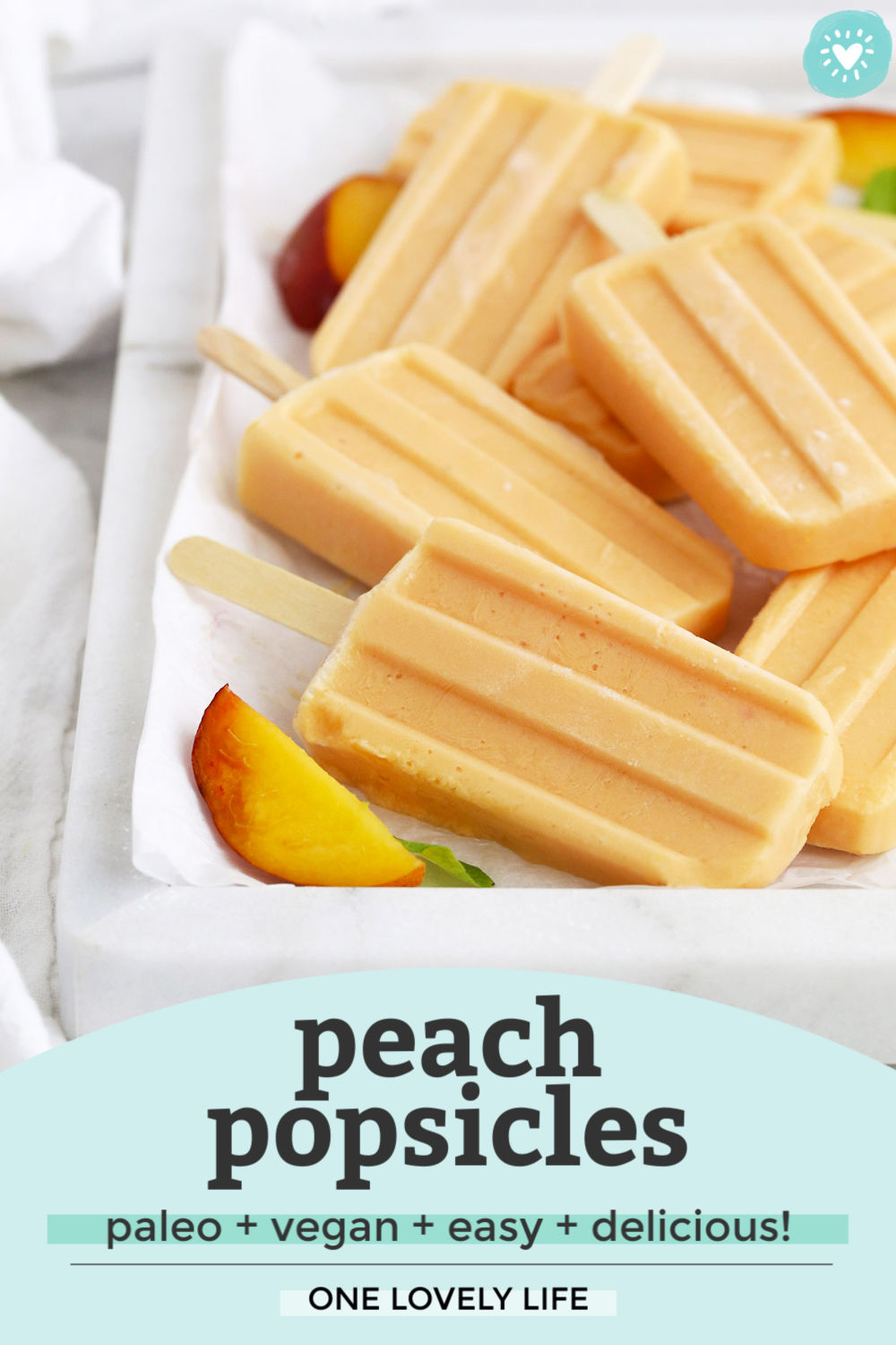 Front view of peach popsicles on a marble serving platter with peach slices and mint leaves with text overly that reads "peach popsicles. paleo + vegan + easy + delicious! One Lovely Life"