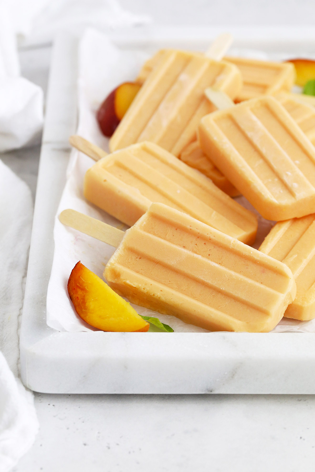 Front view of a marble platter with peach popsicles, peach slices, and mint leaves