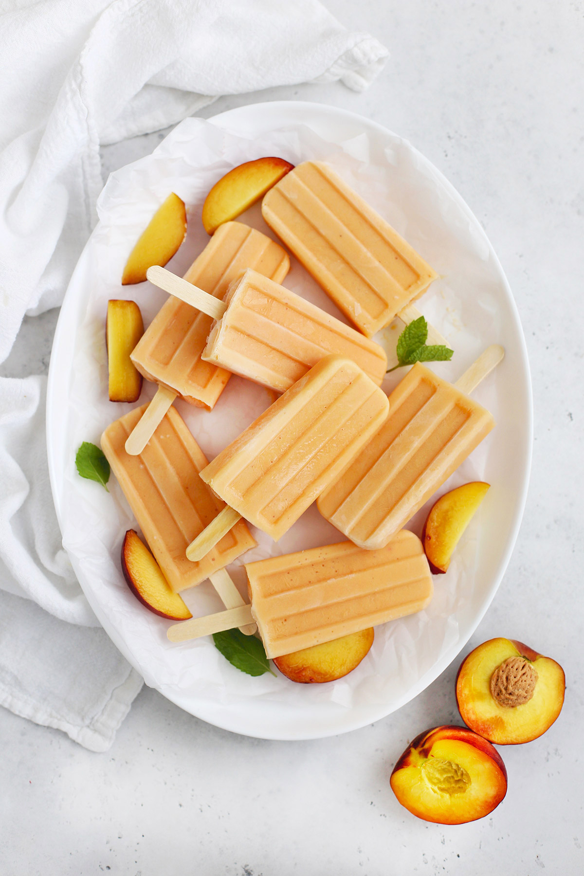 Overhead view of Peach Popsicles on a white platter with peach slices and mint leaves