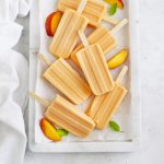 Overhead view of peach popsicles on a marble serving platter with peach slices and mint leaves