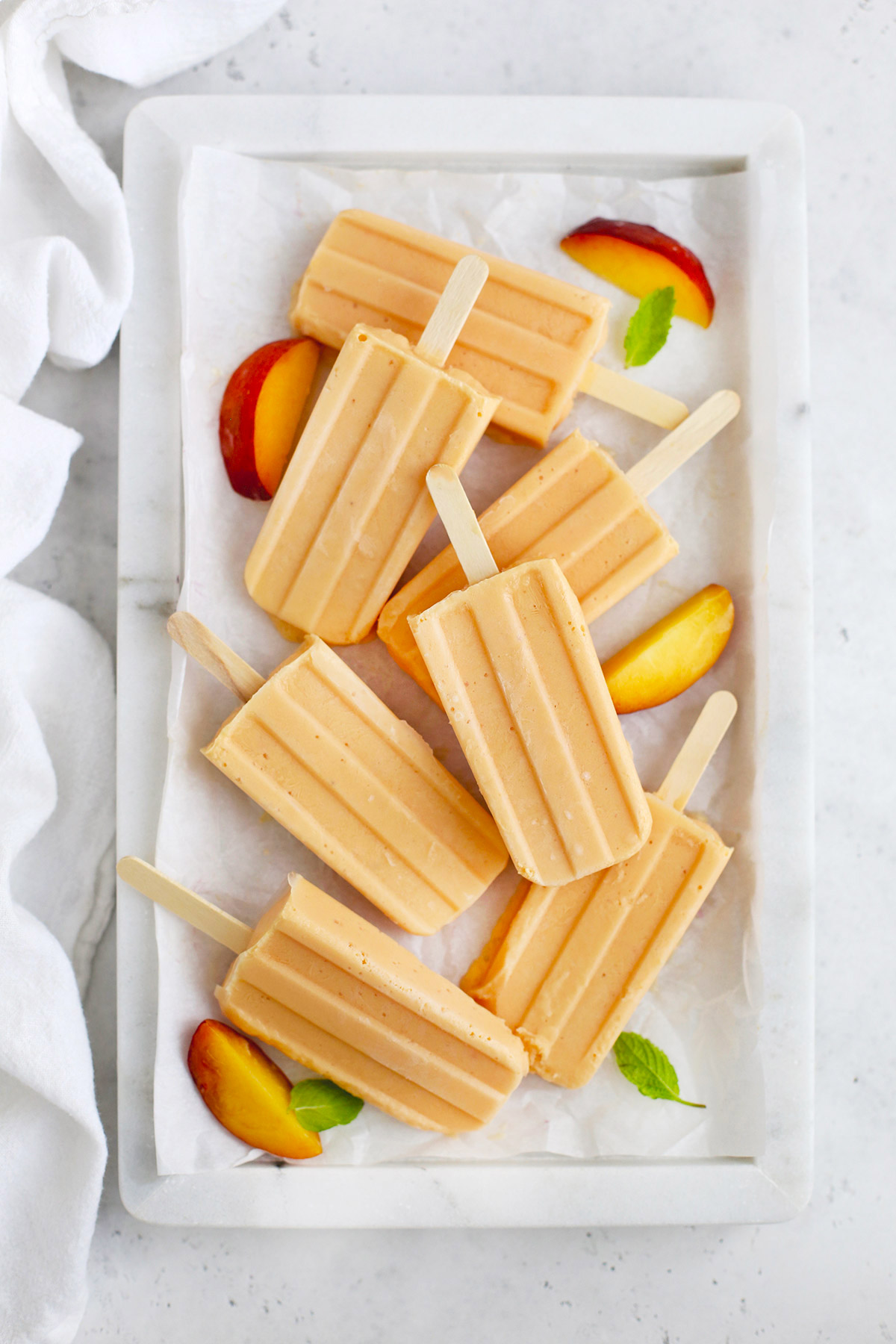 Overhead view of peach popsicles on a marble serving platter with peach slices and mint leaves