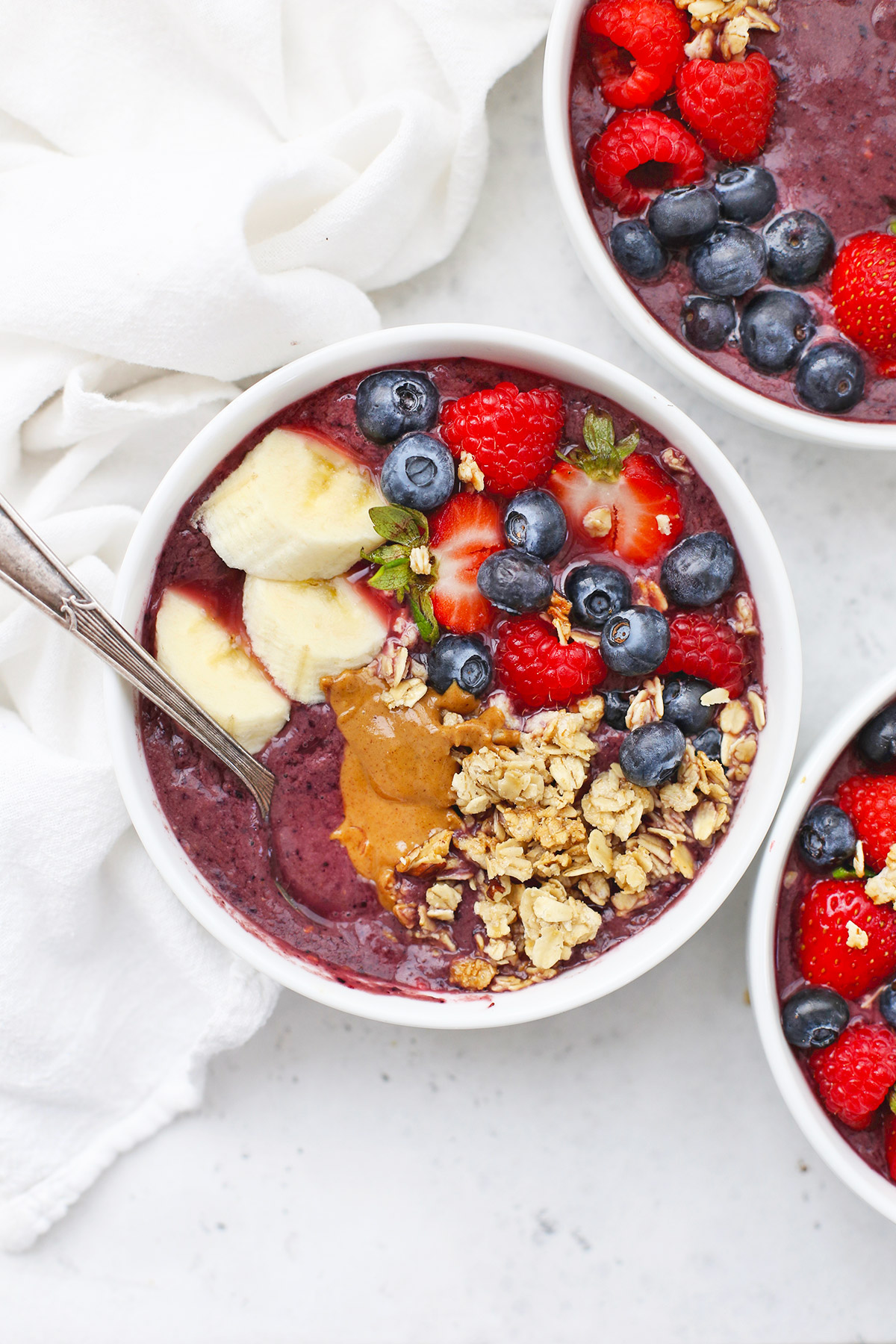 Three Peanut Butter Acai Bowls topped with fresh berries, banana, granola, and peanut butter. 