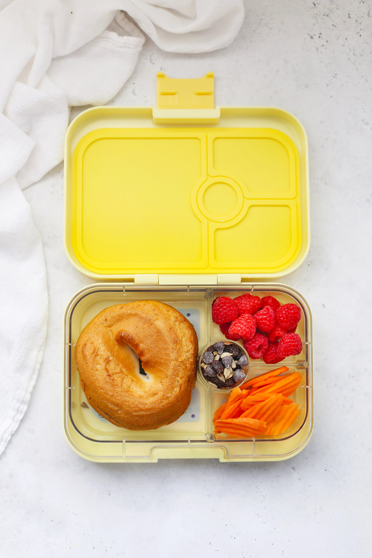 Yellow Yumbox Panino with gluten-free bagel and cream cheese, raspberries, crinkle cut carrots, and trail mix