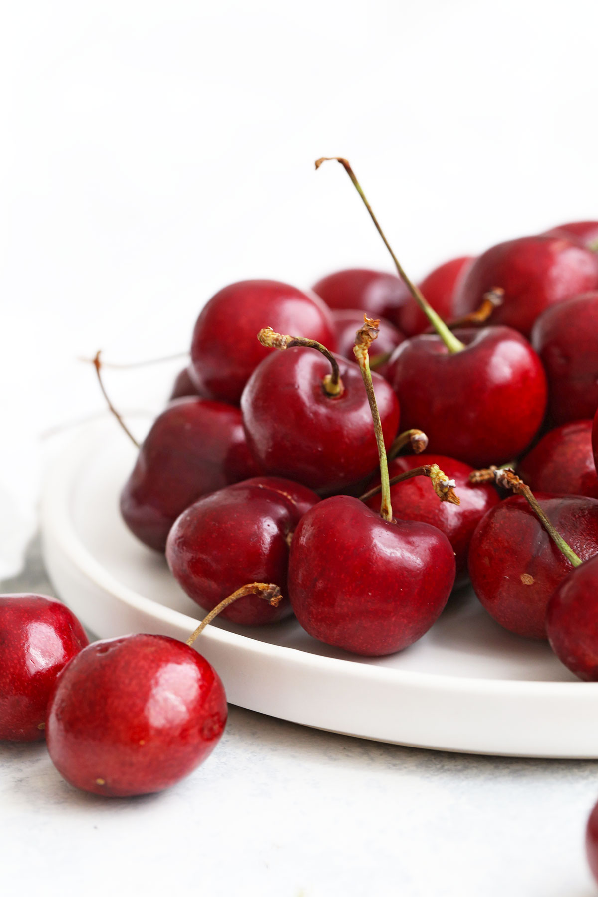 Close up view of sweet cherries on a white plate with a white background. 