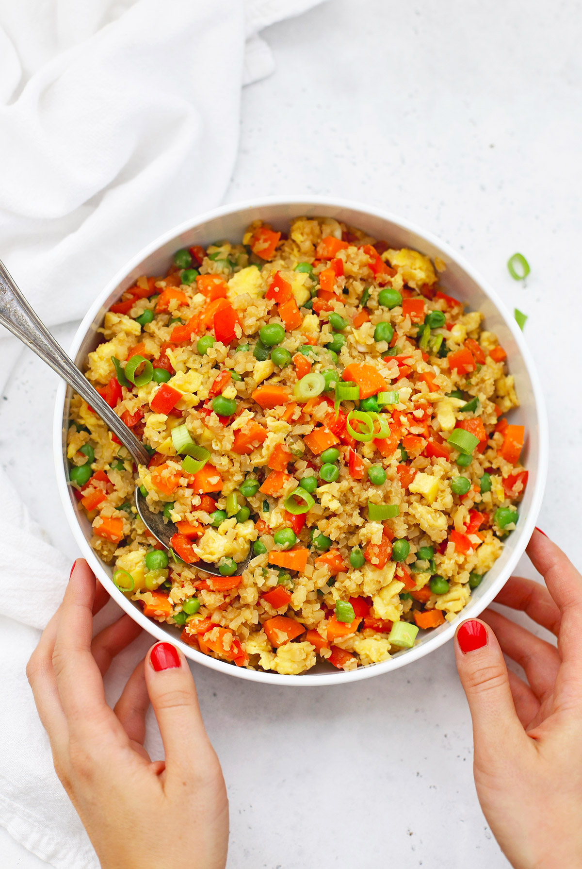 Setting down A large white bowl of gluten-free cauliflower fried rice on a white background. 