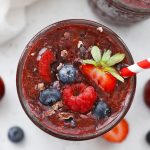 Close up view of a glass of vegan Cherry Berry Smoothie topped with fresh berries and cacao nibs