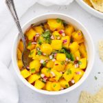 Overhead view of Mango Salsa in a white bowl with tortilla chips on the side