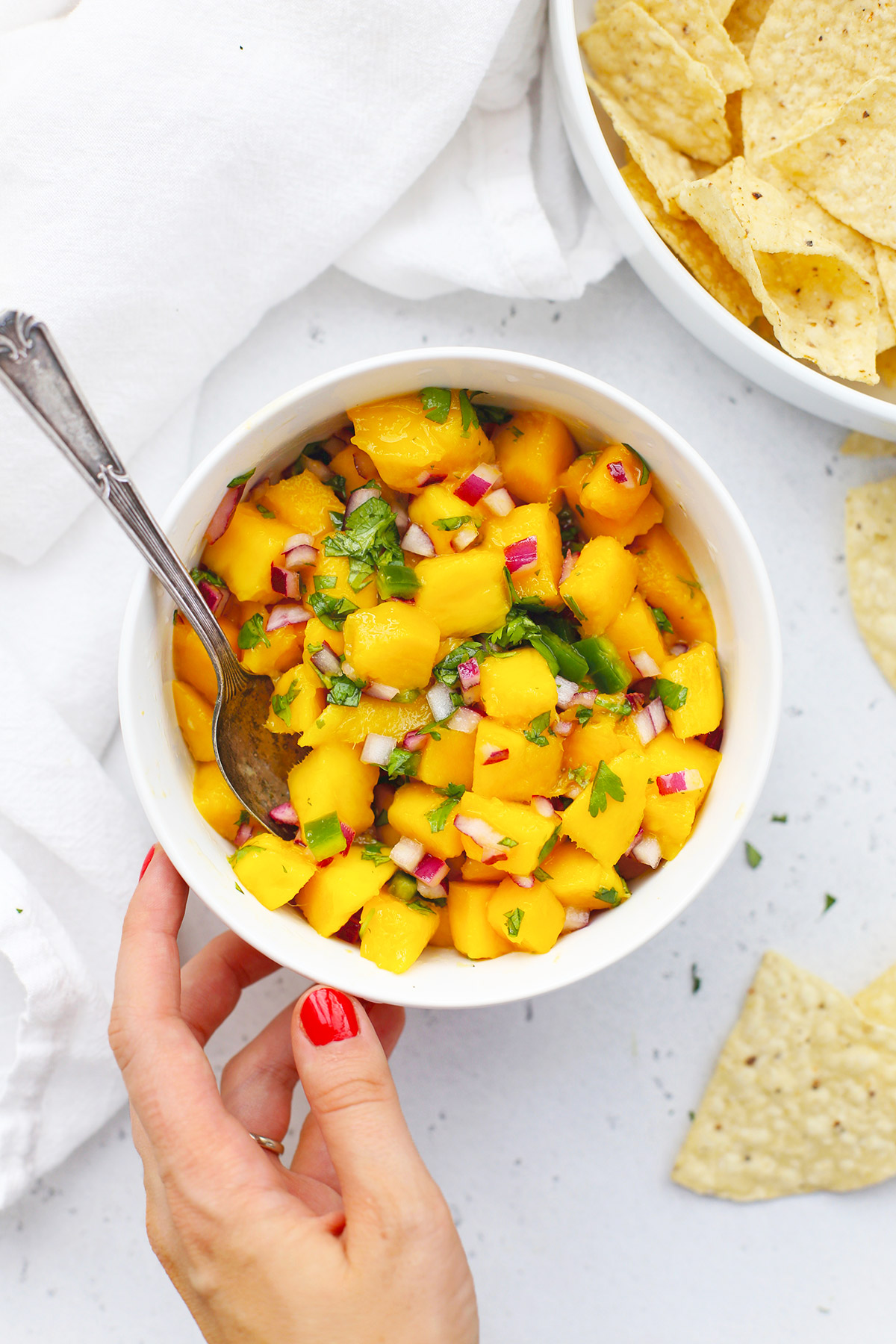 Placing a bowl of fresh mango salsa on a white background with chips