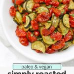 Overhead view of a bowl of simply roasted zucchini and tomatoes with text overlay that reads "vegan + paleo simply roasted zucchini & tomatoes: the seasoning is amazing!"