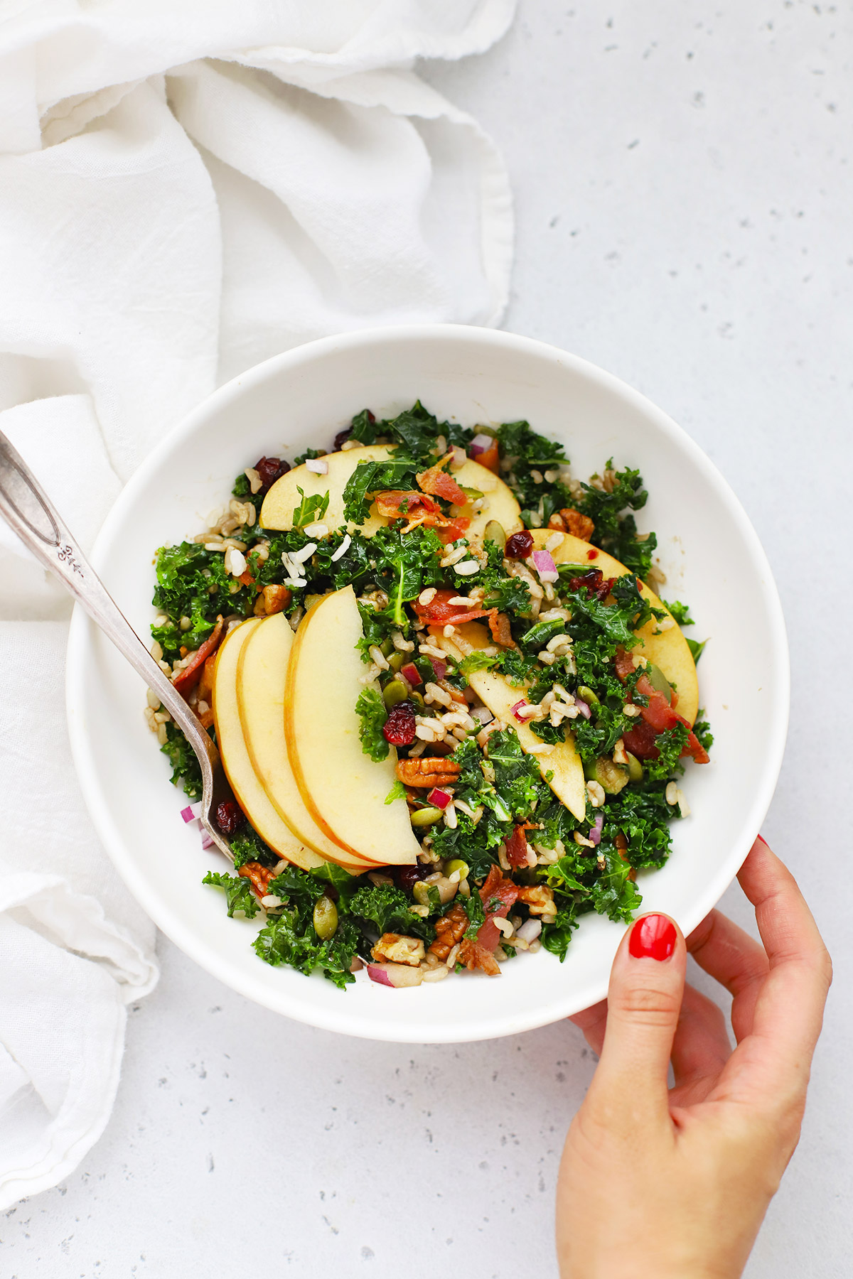 Setting down a bowl of Harvest Apple Kale Salad on a white background