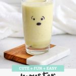 Pineapple Coconut Lime Smoothie in a juice glass with a monster face draw on on it with text overlay that reads "Cute + Fun + Easy Monster Smoothies"