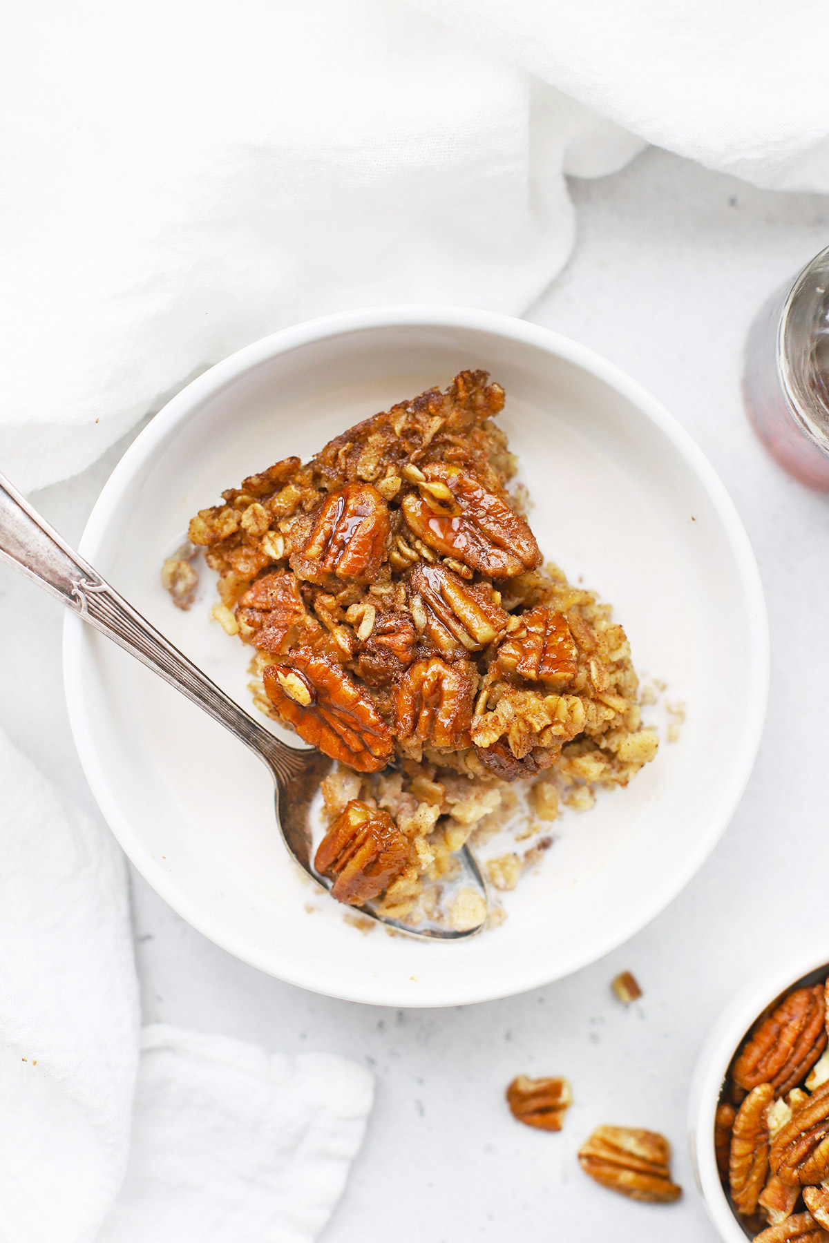 Overhead view of a warm bowl of gluten free pecan pie baked oatmeal served with almond milk