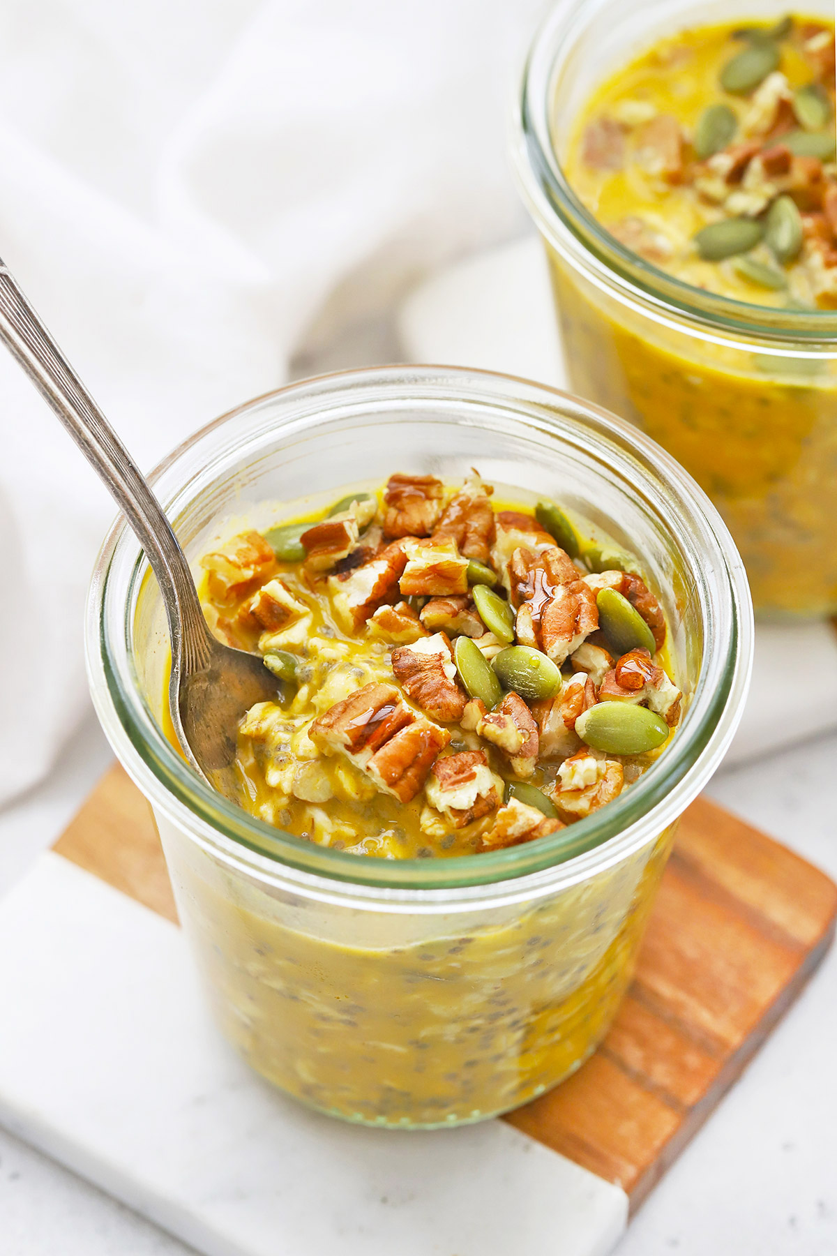 Spoon dipped into a jar of Pumpkin Pie Overnight Oats topped with pecans and pumpkin seeds