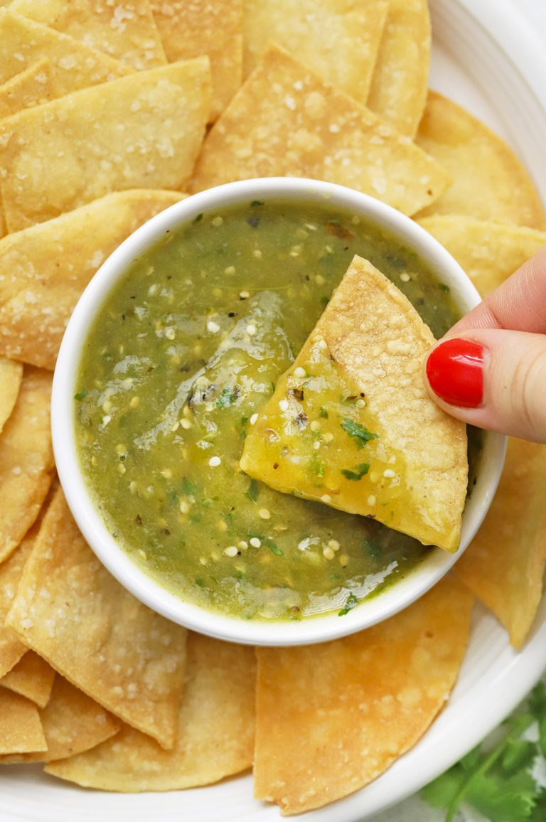 Close up view of a tortilla chip being dipped into homemade salsa verde (green salsa)