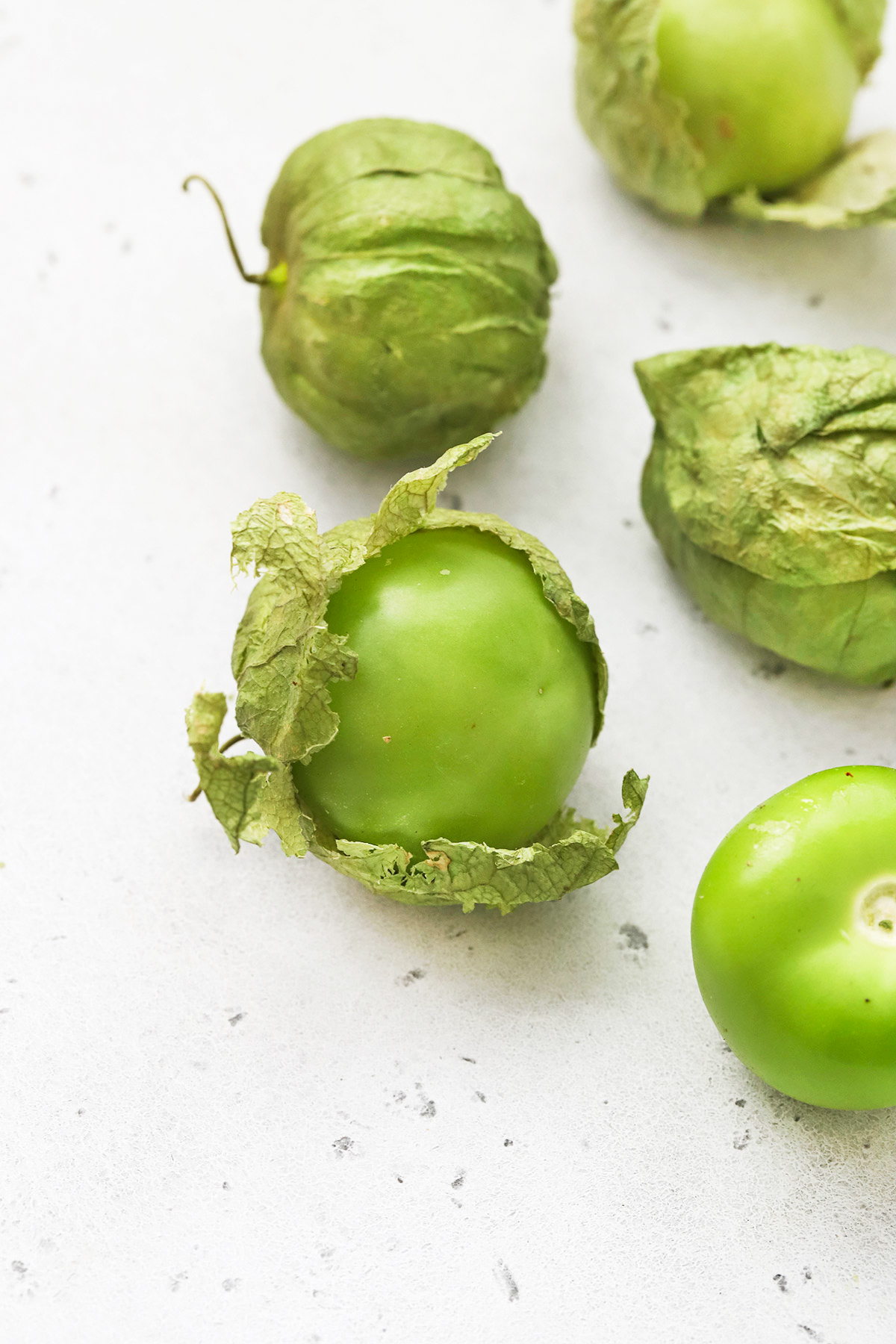Tomatillos being peeled from their husks on a white background