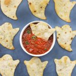 Baked Halloween Ghost Chips on a black background with a bowl of red salsa