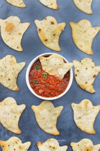 Baked Halloween Ghost Chips on a black background with a bowl of red salsa