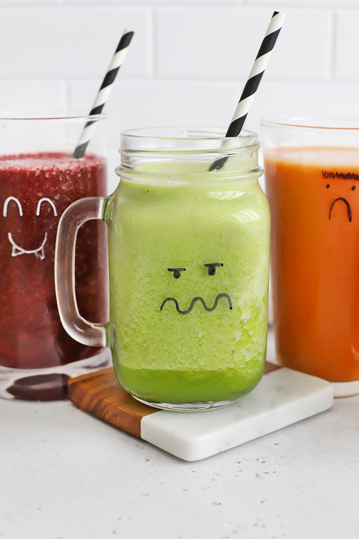 Purple, Green, and Orange Smoothies in glasses with monster faces drawn on them
