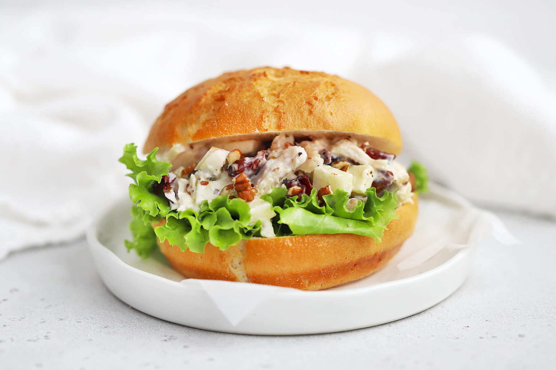 Front view of an apple cranberry chicken salad sandwich made with a gluten-free bun on a white plate.