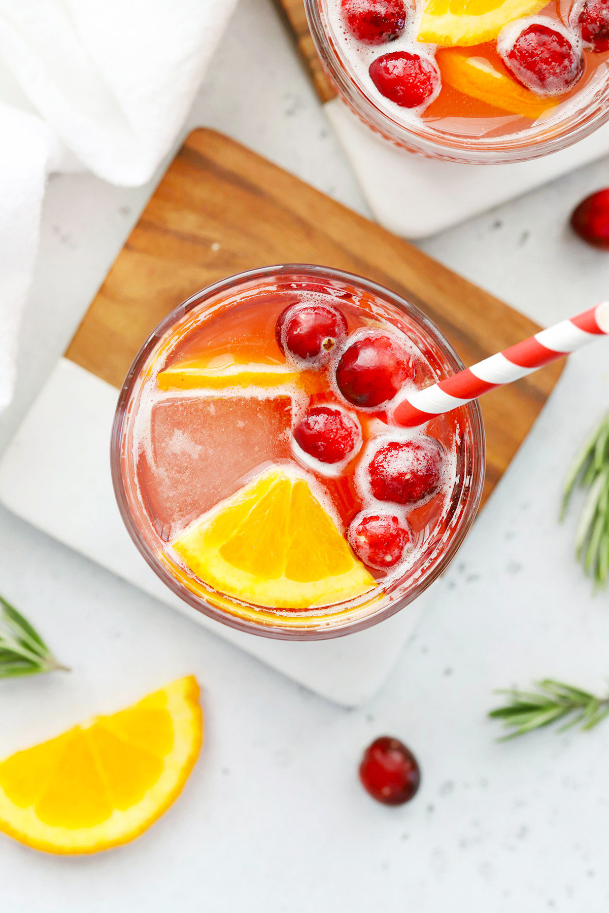 Overhead view of a Cranberry Cider Mocktail garnished with orange wedges and cranberries on a marble and wood coaster on a white background