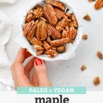 Hand setting down a speckled bowl of naturally sweetened maple candied pecans on a white background with text overlay that reads "Paleo + Vegan Maple Candied Pecans. Naturally Sweetened + Delicious!"