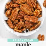 Close up view of Overhead view of a speckled bowl of naturally sweetened maple candied pecans on a white background with text overlay that reads "Paleo + Vegan Maple Candied Pecans. Naturally Sweetened + Delicious!"