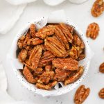 Overhead view of a speckled bowl of naturally sweetened maple candied pecans on a white background