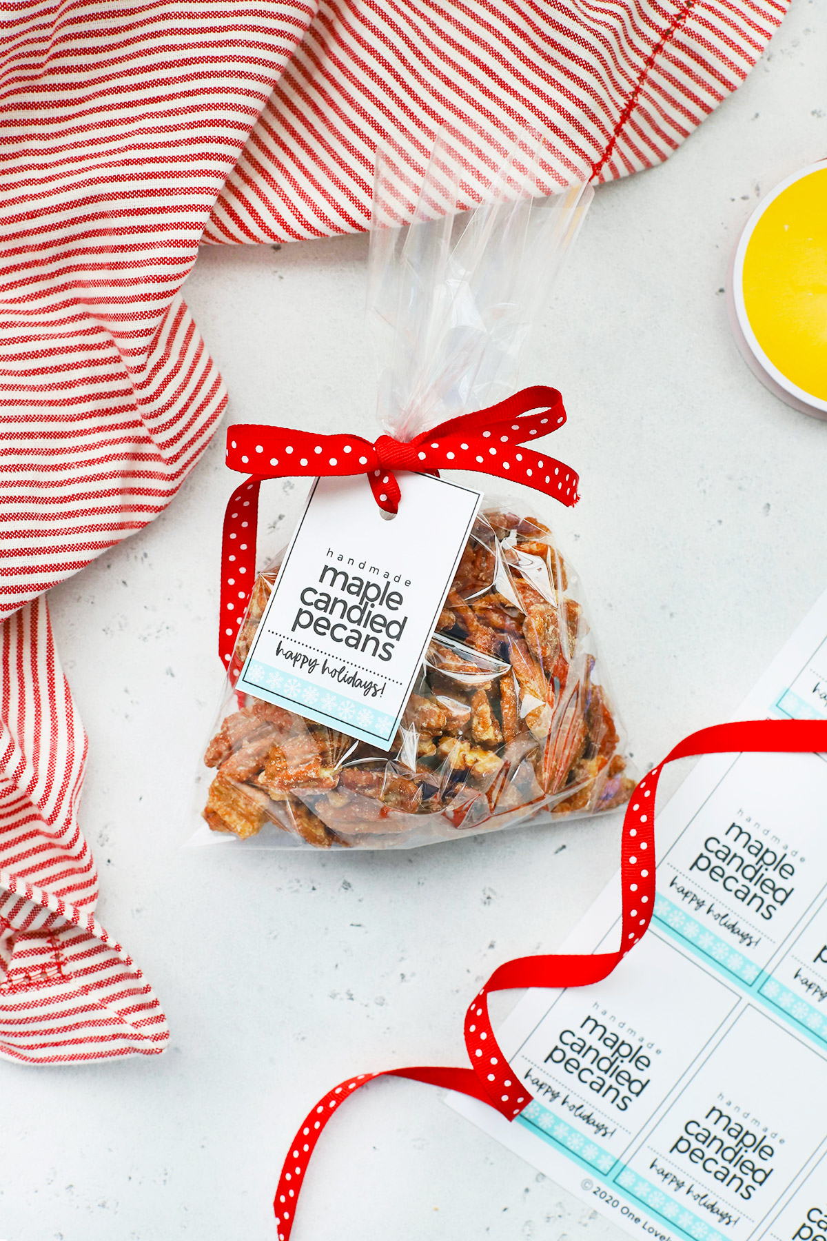 Overhead view of a gift back of naturally sweetened maple candied pecans with a free printable gift tag and red polka dot ribbon