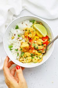 Setting down a bowl of coconut shrimp curry on a white background