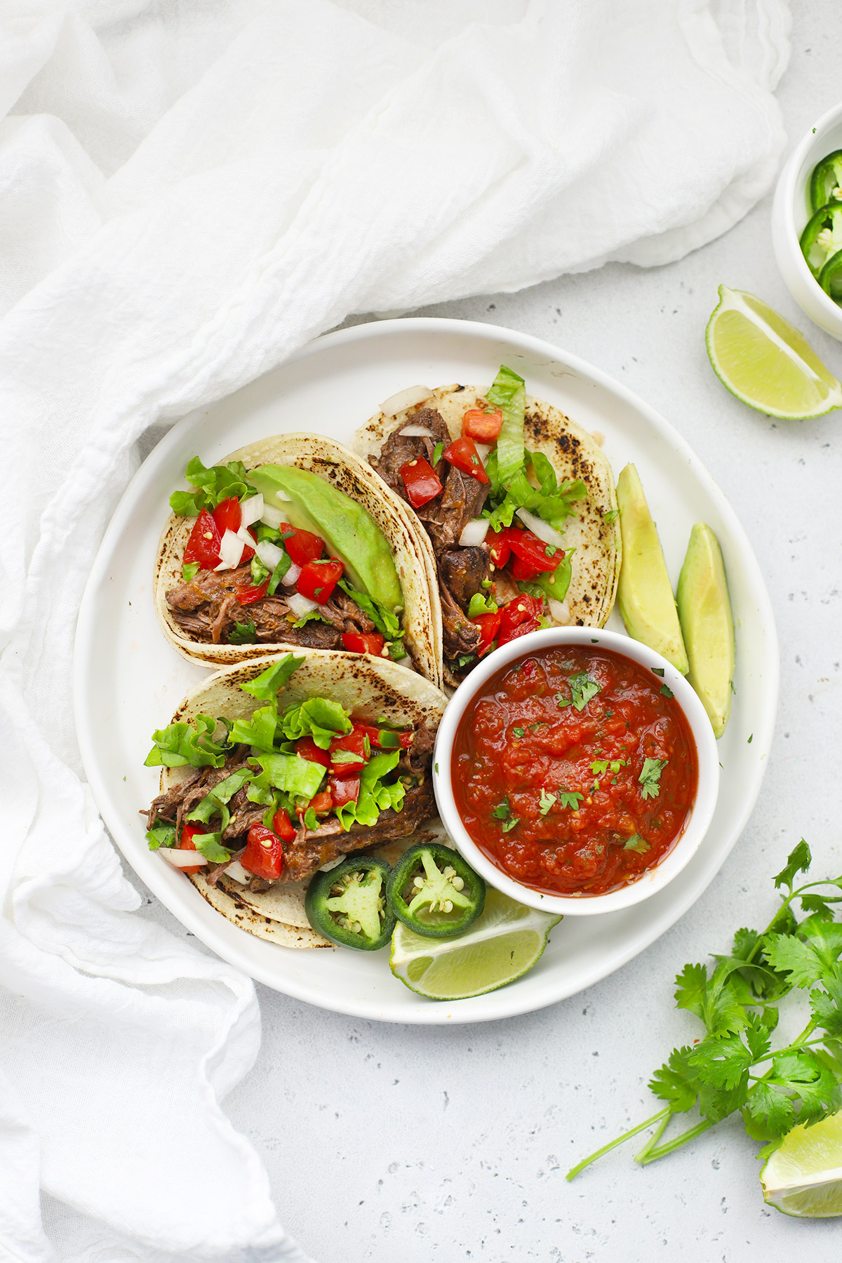 Overhead view of a plate of slow cooker barbacoa beef tacos with salsa and avocado