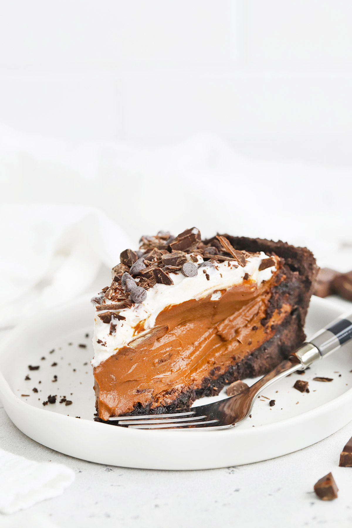 A slice of vegan chocolate pie with chocolate cookie crust on a white plate. 