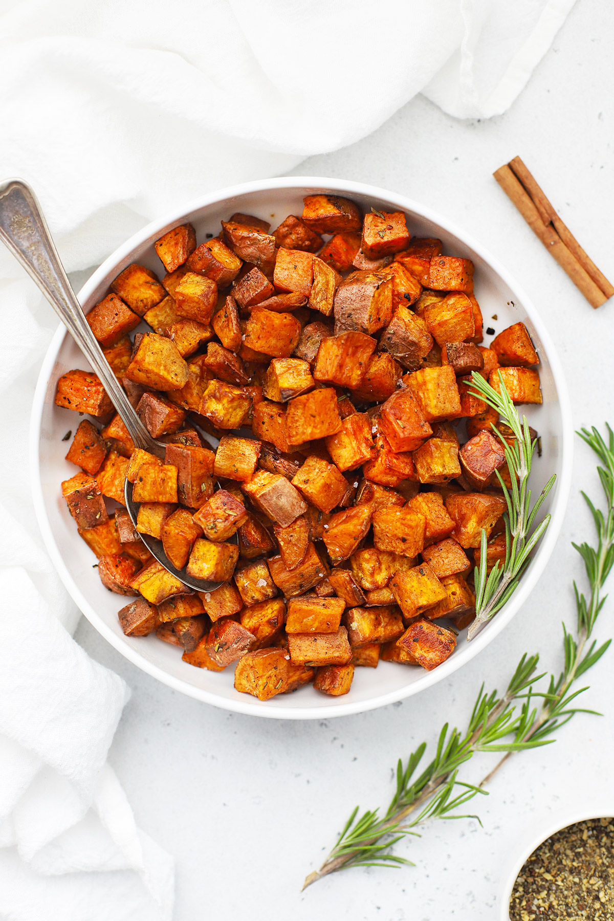 Overhead view of Cinnamon Rosemary Sweet Potatoes in a white bowl on a white background