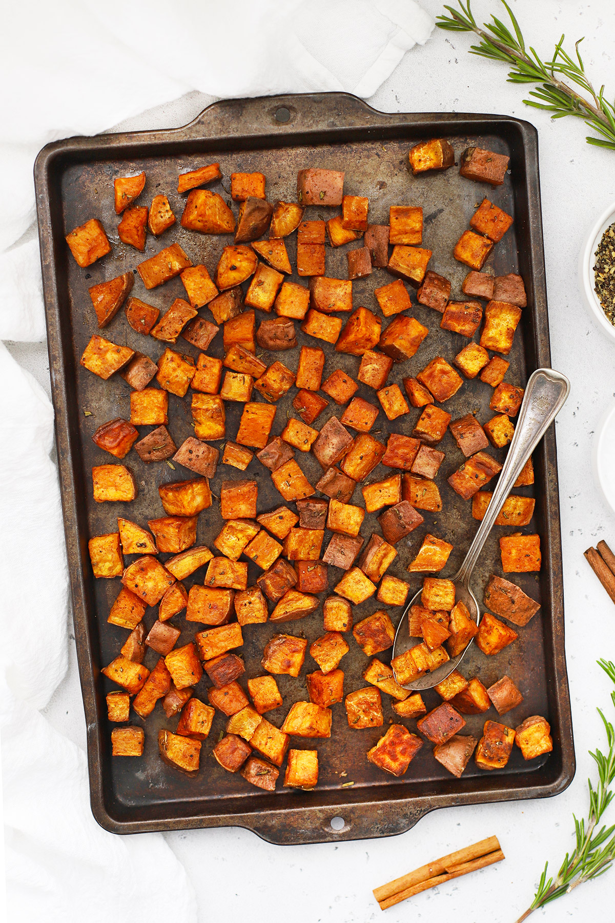 Overhead view of cinnamon roasted sweet potatoes on a baking sheet placed on a white background