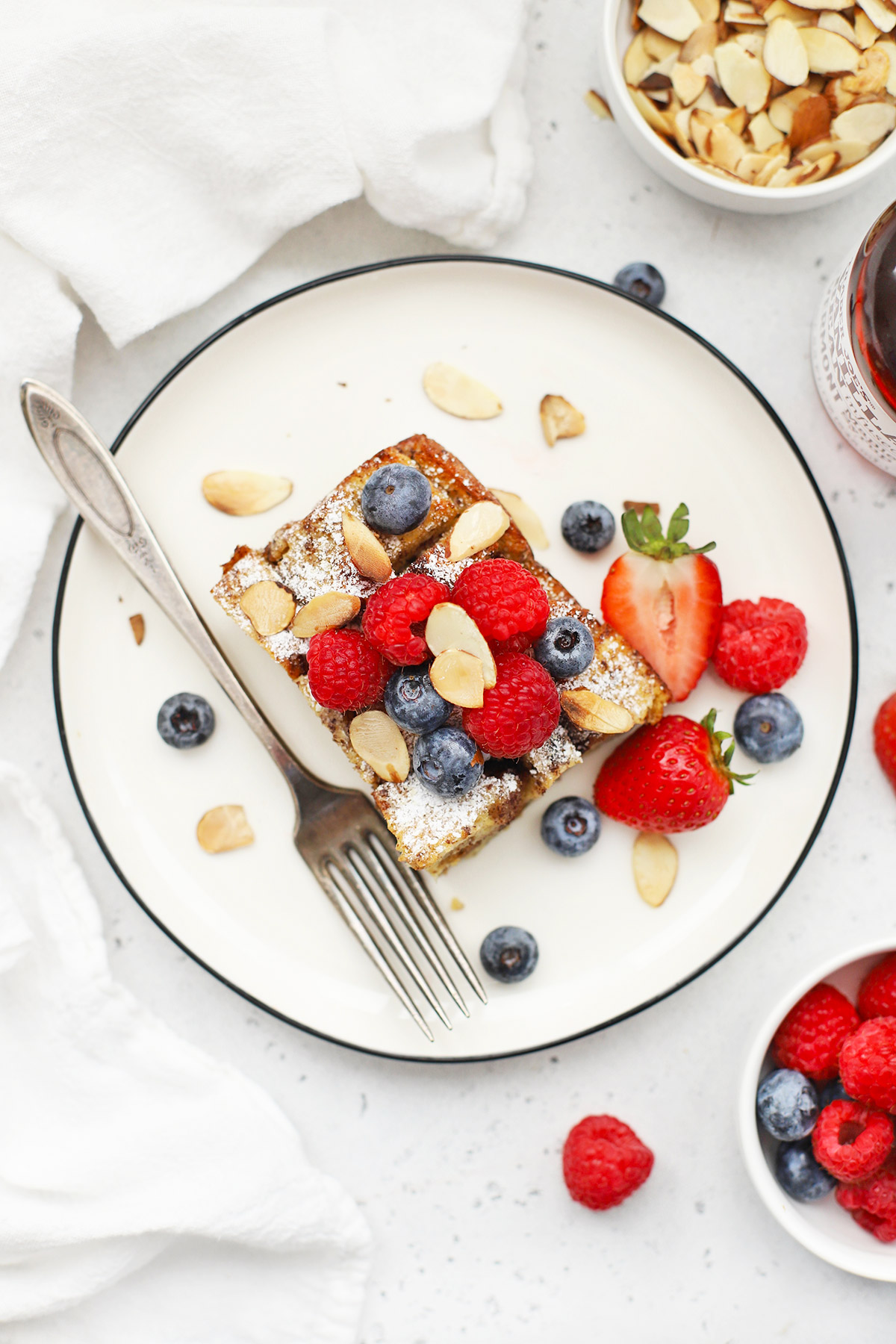 Overhead view of a slice of gluten-free french toast casserole on a white plate topped with berries and almonds