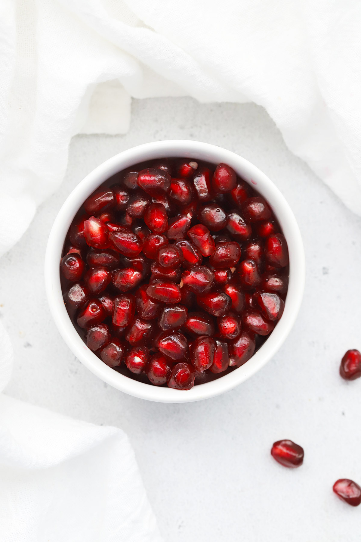 Overhead view of pomegranate seeds in a white bowl on a white background