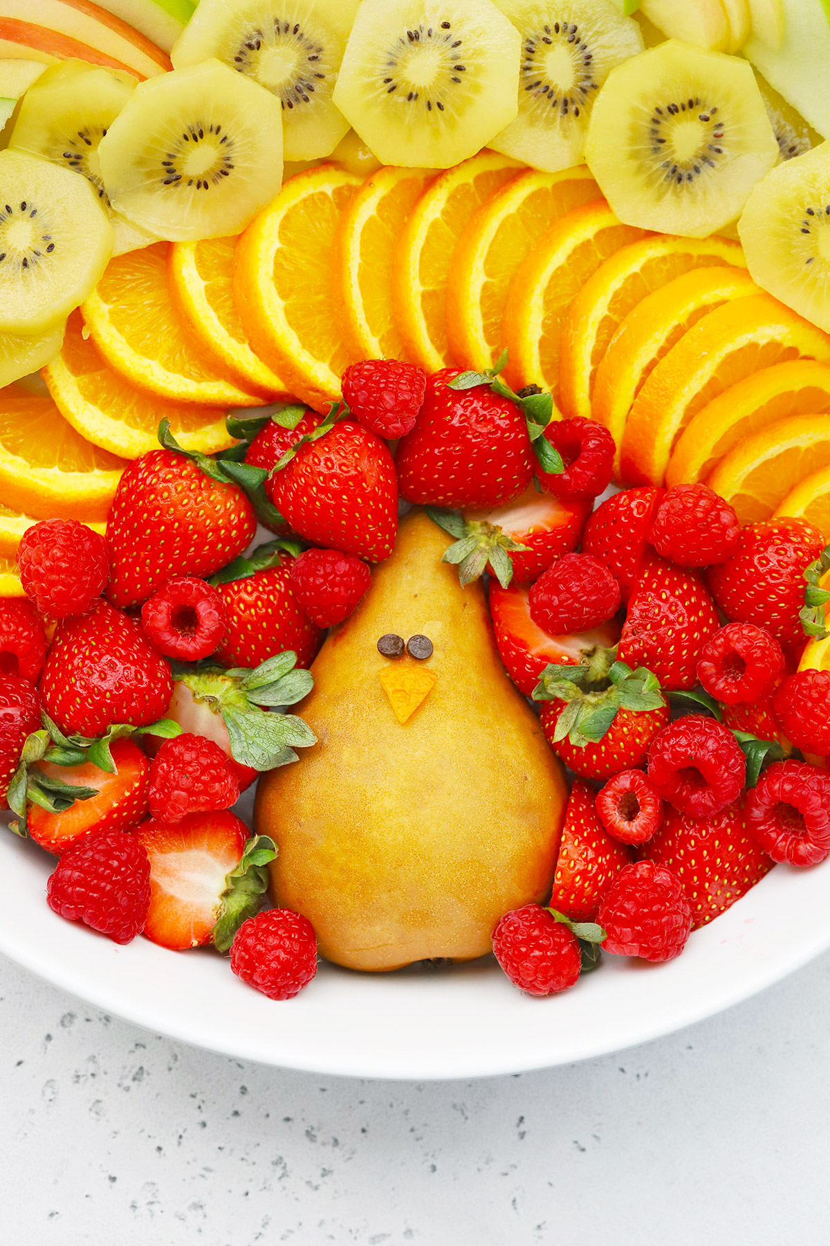 Overhead view of Thanksgiving Fruit Plate shaped like a turkey with text overlay that reads "Cute + Easy Thanksgiving Turkey Fruit Plate: Simple + Fun + Adorable!"