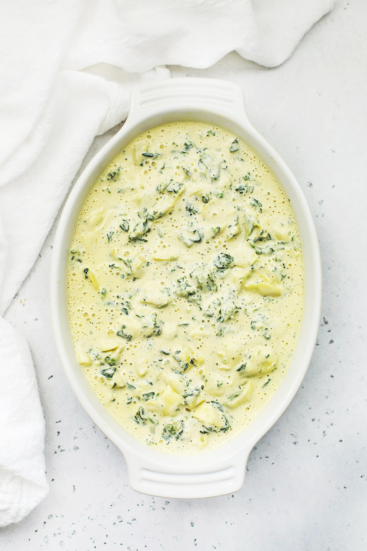Overhead view of a baking dish of vegan spinach artichoke dip ready to go into the oven