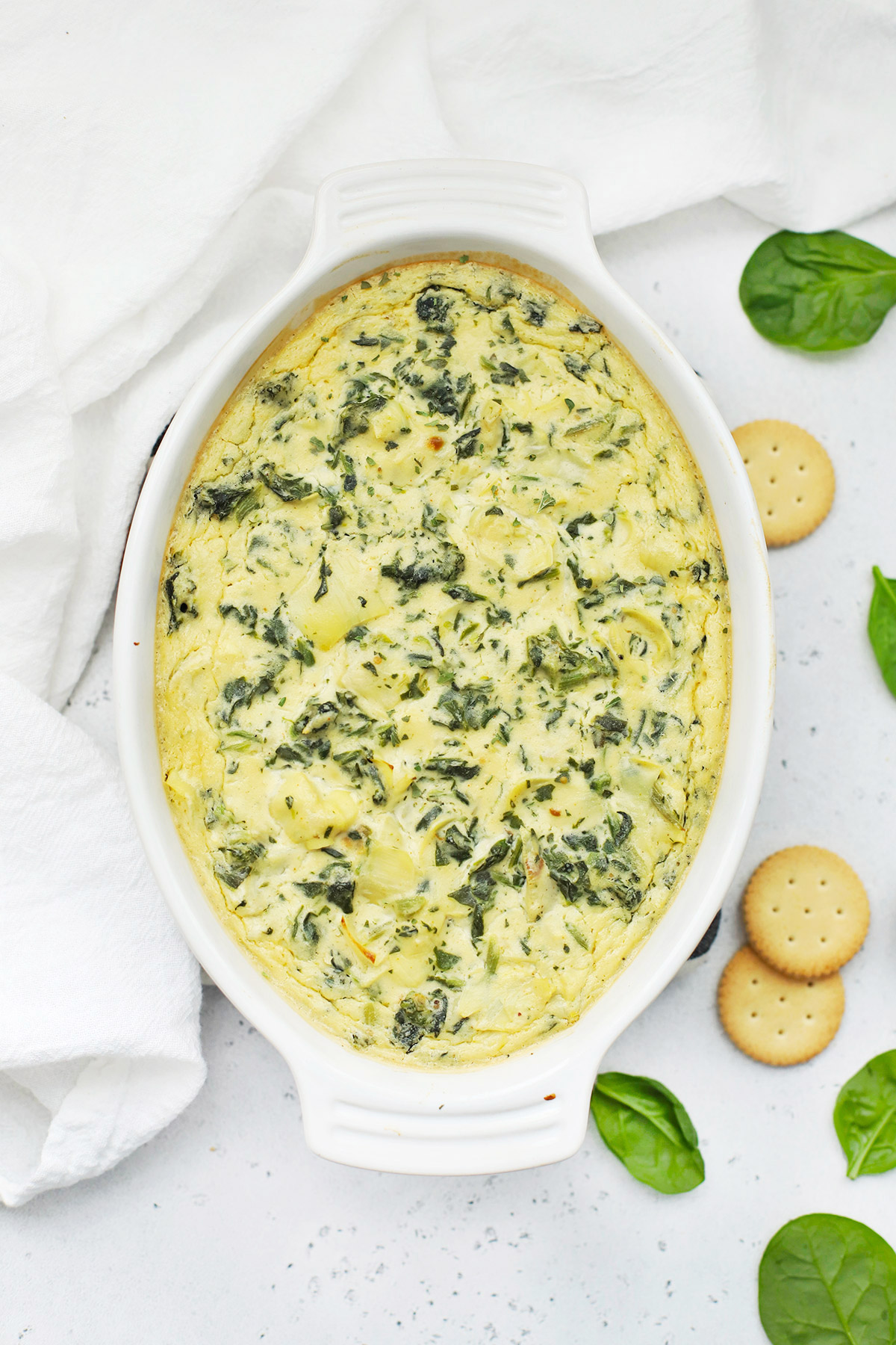 Overhead view of dairy free vegan spinach artichoke dip on a white background with gluten-free crackers